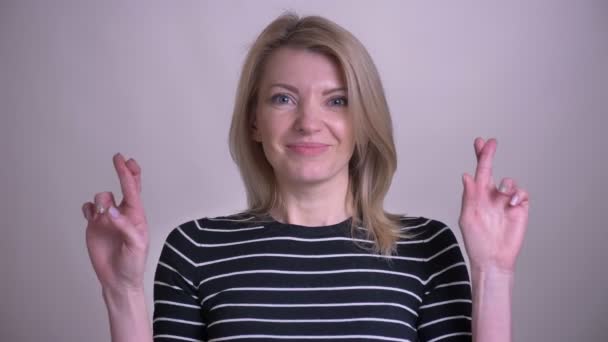 Портрет крупным планом взрослой привлекательной белокурой белокурой женщины со скрещенными пальцами, смотрящей в камеру на белом фоне — стоковое видео