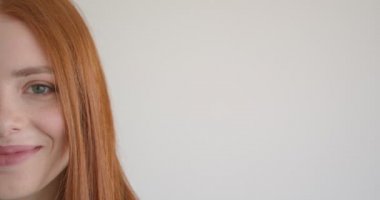 Beyaz arka planda kameraya gülümseyerek ve dikkatle izleyen güzel zencefil modelinin yarım yüz portresi.