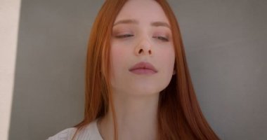 Beyaz duvara yaslanmış güneş iyakalarken kamera ile flört Pretty genç zencefil modeli.