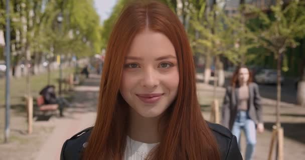 Hermosa chica de jengibre en chaqueta de cuero posando sonriente en la cámara sobre fondo de callejón verde . — Vídeo de stock