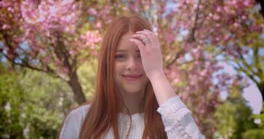 Beyaz bluz büyüleyici zencefil kız öğrenci rüya gibi sola ve pembe çiçek bahçesinde kamera içine izlerken.