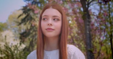 Beyaz bluz büyüleyici zencefil kız pembe çiçek bahçesinde pozlar değişen kamera içine pozlar.