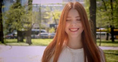 Kırmızı başlı kız kameraya yürüme ve yeşil parkta memnuniyetle içine gülümseyerek.