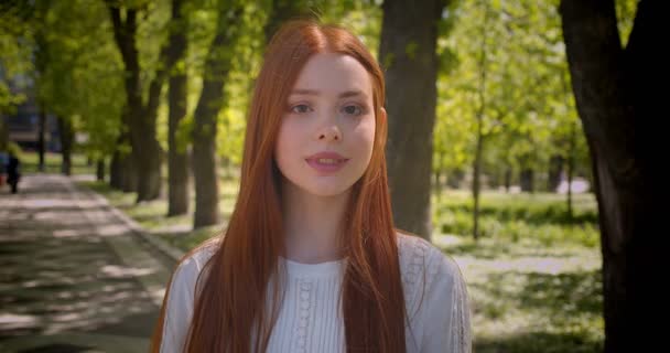 Retrato de menina de gengibre bonito se vira para a câmera sorrindo sendo feliz em câmera no parque verde . — Vídeo de Stock