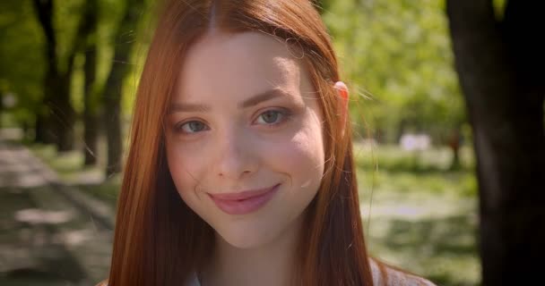 Close-up retrato de menina de gengibre bonito posando bonita e ternamente em câmera no parque verde . — Vídeo de Stock
