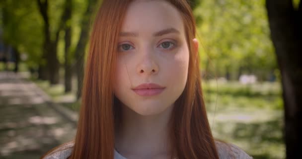 Close-up retrato de menina de gengibre bonito assistindo com calma seriedade em câmera no parque verde . — Vídeo de Stock