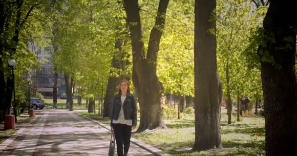 Full storlek porträtt av rödhövdad vacker flicka som går längs gröna gränd är lugn och drömmande. — Stockvideo
