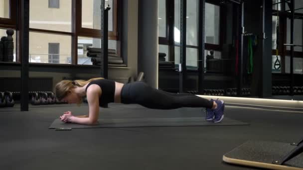 Ung idrottsflicka står i planka med sin mobiltelefon ligger i närheten i gymmet. — Stockvideo