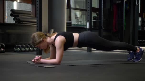 Ung idrottsflicka gör planka med sin mobiltelefon ligger i närheten i gymmet. — Stockvideo