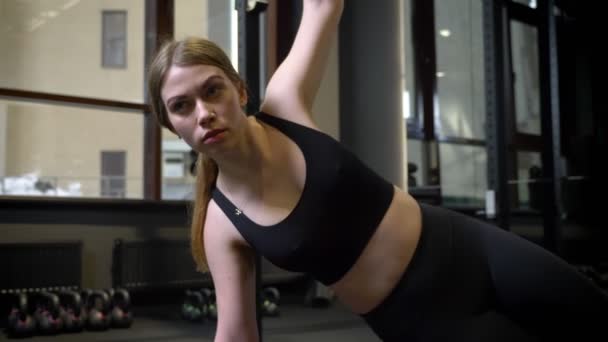 Circlind aroung syn på koncentrerad sportsgirl stående i SIDOPLANKA med sin telefon som ligger i närheten i gymmet. — Stockvideo