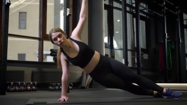 Jonge geconcentreerde sportmeisje staat in de zij plank met haar armen wijd open in de sportschool. — Stockvideo