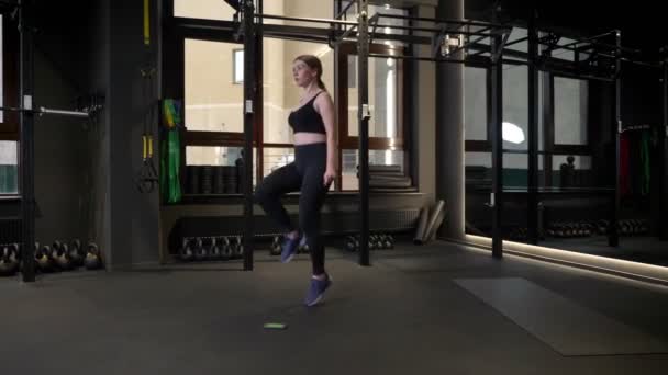 Joven deportista corriendo con las rodillas levantadas con su teléfono celular tirado cerca en el gimnasio . — Vídeos de Stock