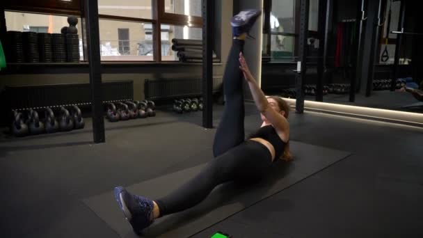 Joven y cansada deportista haciendo levantamiento cruzado de pierna estando concentrada y motivada en gimnasio . — Vídeos de Stock