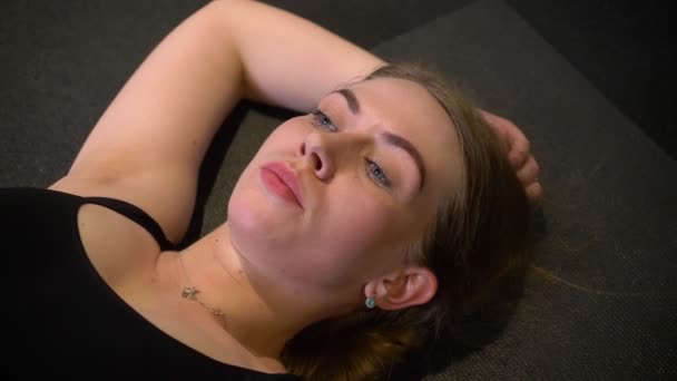 Κοντινό-up πορτρέτο του ιδρωμένο και κουρασμένο αθλητικό κορίτσι που βρίσκεται στο karrimat είναι κουρασμένοι και εξαντλημένοι στο γυμναστήριο. — Αρχείο Βίντεο