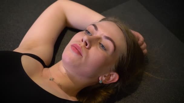 Gros plan portrait d'une sportive fatiguée et en sueur allongée sur un karrimat fatiguée et épuisée au gymnase . — Video