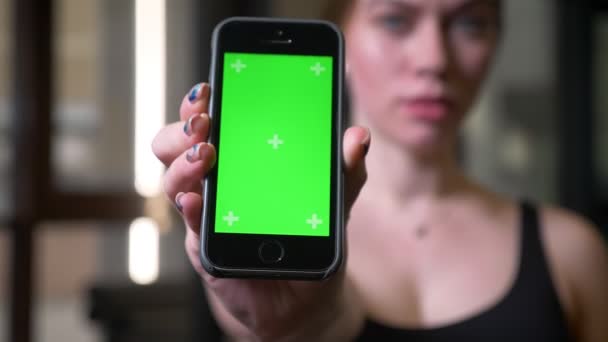 Close-up shot of blurred sportswoman holding cellphone with chromakey green screen in gym. — Stock Video