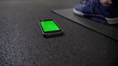 Spor salonunda karrimat üzerinde spor ayakkabıları yanında yatan renkyeşil ekran ile akıllı telefon görünümü etrafında daire.
