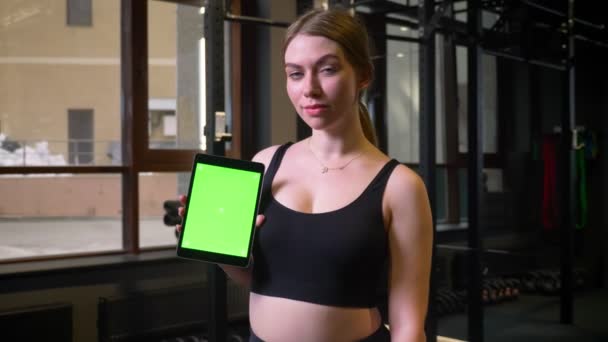 Sportswoman z kucyk pokazuje tablet z Chromakey zielony ekran w aparacie jest spokojny i uśmiechnięty w siłowni, — Wideo stockowe