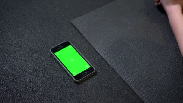 Das Handy mit grünem Chromakey-Bildschirm, das in der Nähe der Kaimatte in der Turnhalle liegt. — Stockvideo