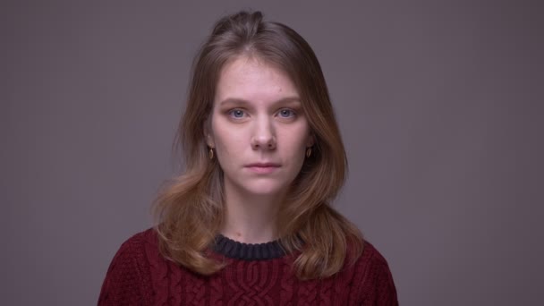 Portret van een jonge vrouwelijke student die vredig in de camera op een grijze achtergrond kijkt. — Stockvideo