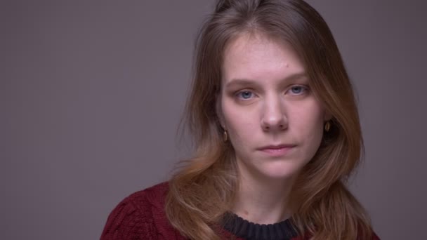 Close-up portret van jonge vrouwelijke student die onhandig kijkt naar de camera die wordt gestrest op de grijze achtergrond. — Stockvideo