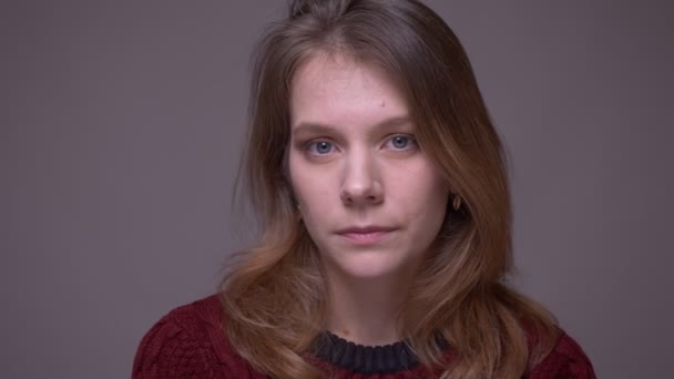 Close-up portret van jonge vrouwelijke student krijgt verward kijken naar camera onhandig op grijze achtergrond. — Stockvideo