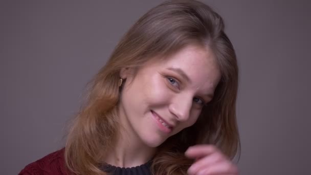 Portret van jonge vrouwelijke student speelt met haar haar flirten met camera op grijze achtergrond. — Stockvideo
