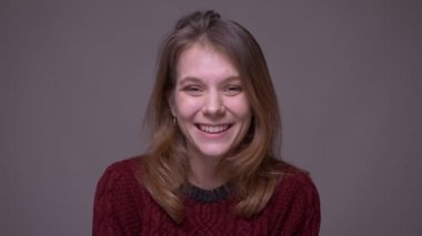 Pretty genç kız öğrenci dalgalar kameraya el mutlu olmak ve gri arka planda şaşırttı.