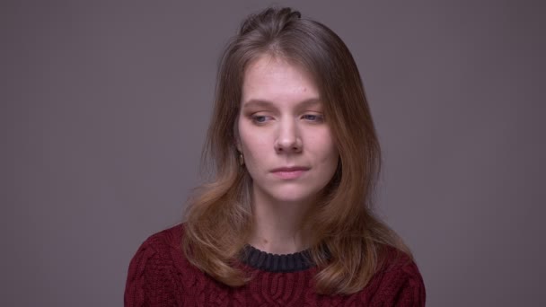 Retrato de una joven estudiante deprimida mirando miserablemente a la cámara sobre un fondo gris . — Vídeo de stock