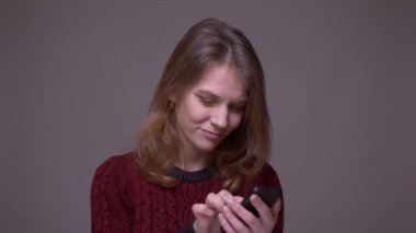 Genç kız öğrenci akıllı telefondan fotoğraf aşırıyor ve gri arka planda duygusal tepki veriyor..