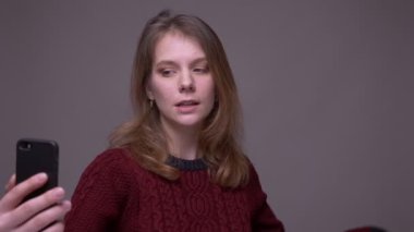 Genç kız öğrenci gri arka planda akıllı telefondan video şapkayla konuşuyor..