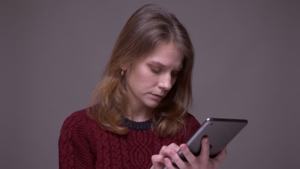 Młoda studentka patrząc poważnie na tabletkę jest uważny i koncentruje się na szarym tle. — Wideo stockowe