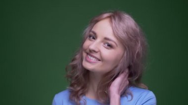 Dalgalı uzun saçlı güzel model yeşil renk arka plan üzerinde kameraya utangaç poz saçları ile oynar.