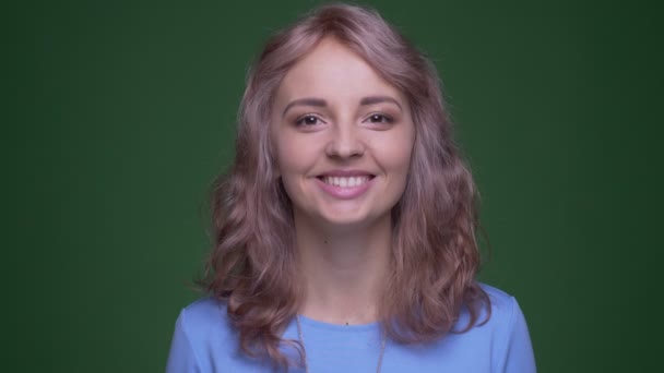 Beautiful model with wavy long hair smiles sincerely and happily into camera on green chroma background. — Stock Video
