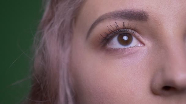 Close-up half face shot of beautiful model watches upwards and into camera being calm on green background. — Stock Video