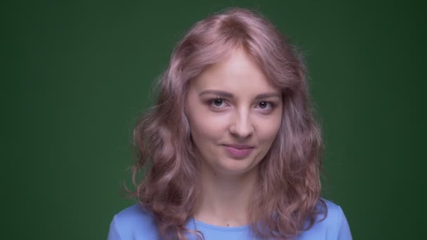 Bellissimo modello con i capelli lunghi ondulati orologi timidamente in macchina fotografica su sfondo cromatico verde . — Video Stock