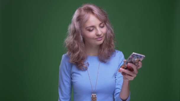緑のクロマの背景にスマートフォン上でセルフを作る波状の長い髪の笑顔を持つ美しいモデル. — ストック動画