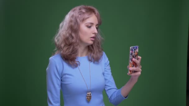 Όμορφο μοντέλο με κυματιστά μακριά μαλλιά που έχουν ένα βιντεοκλήσεων στο smartphone σε πράσινο φόντο αποχρώσεων. — Αρχείο Βίντεο