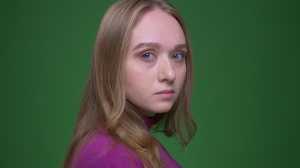 Портрет прекрасной рыжей студентки поворачивается к камере, спокойно глядя в нее на зеленом фоне хромы . — стоковое видео
