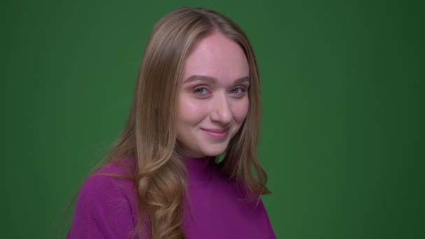 Pretty ginger student watching with shy smile into camera on green chroma background. — Stock Video