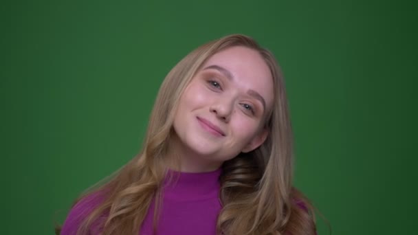 Pretty ginger female student shows tongue and smiling joyfully into camera on green chroma background. — Stock Video