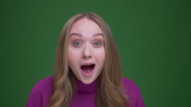 Pretty ginger female student being amused and happy watches into camera on green chroma background. — Stock Video