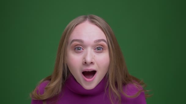 Pretty ginger female student being amused and happy jumps actively on green chroma background. — Stock Video