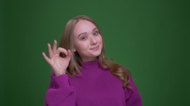 Pretty zencefil kız öğrenci yeşil renk arka plan üzerinde başarı ve mutluluk göstermek için ok jest yapar. — Stok video