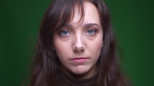 Portret młodego brunetka studentka ogląda ze spokojem smutek w aparacie na zielonym tle. — Wideo stockowe
