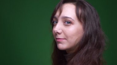 Genç esmer kız öğrenci kameraya döner ve yeşil arka planda içten ve mutlu bir şekilde gülümser..