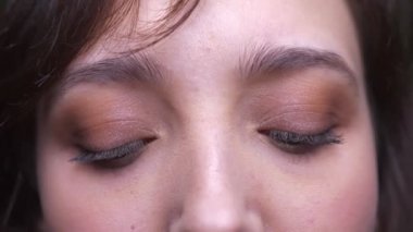 Yeşil arka planda kameraya dikkatle izleyen genç esmer kız öğrencinin yakın çekim göz portresi.