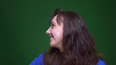 Genç esmer bayan öğrenci yeşil arka planda neşeli ve garip bir şekilde gülümsüyor..