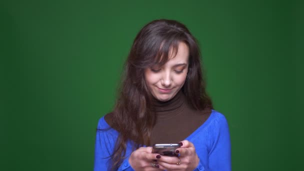 Mladá brunetka studentka pracující pozorně a vážně s chytrým telefonem na zeleném pozadí. — Stock video