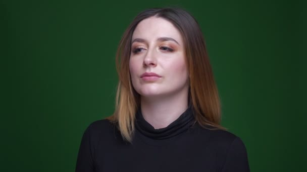 Portrait of young businesswoman with chestnut hair watching seriously into camera and nodding on green background. — Stock Video